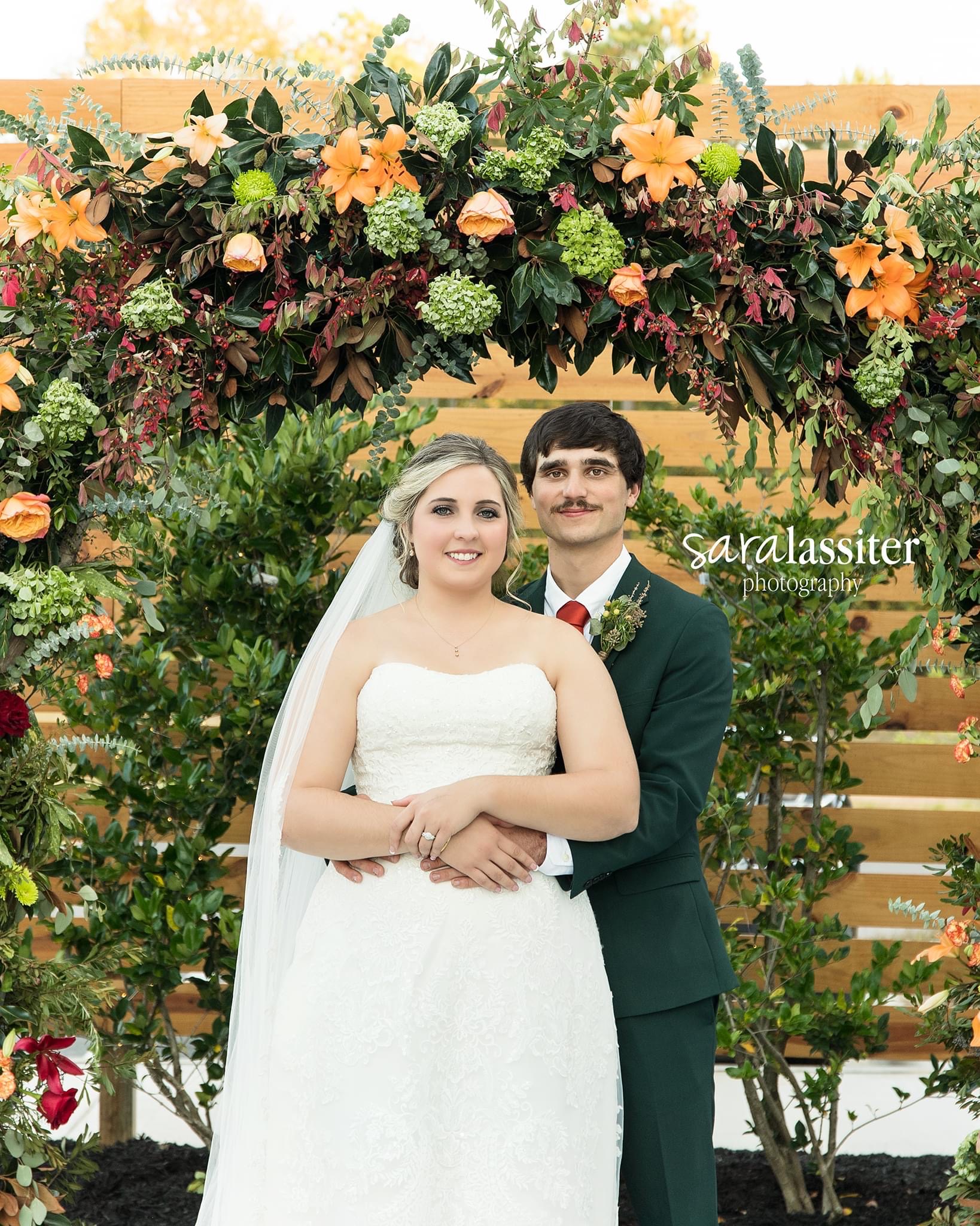 Bride and groom beneath a colorful floral wedding arch